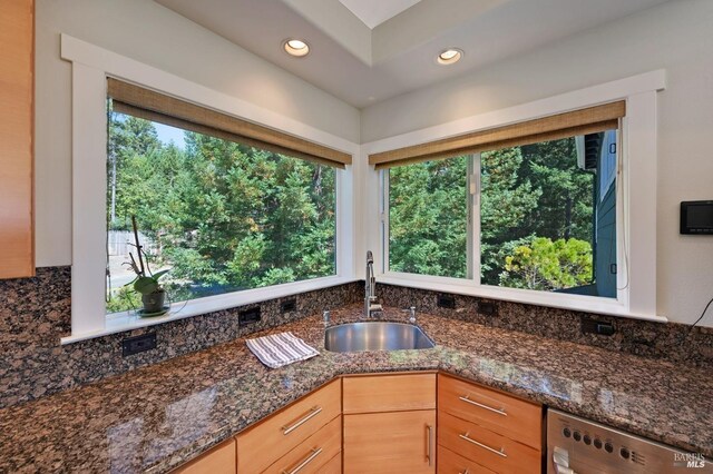 kitchen with light brown cabinets, sink, dishwasher, dark stone countertops, and decorative backsplash