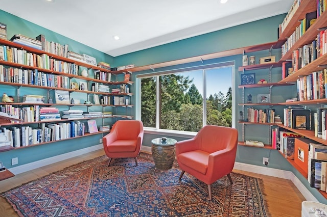 sitting room featuring recessed lighting, wall of books, and baseboards