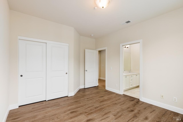 unfurnished bedroom with light wood-type flooring, ensuite bath, and a closet