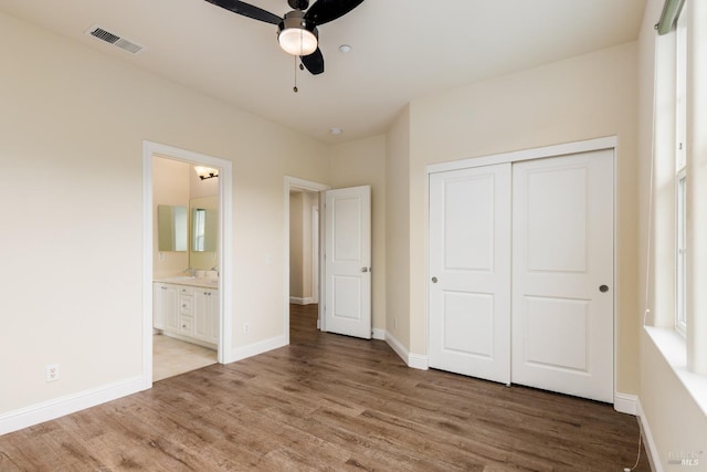 unfurnished bedroom with connected bathroom, hardwood / wood-style floors, ceiling fan, and a closet