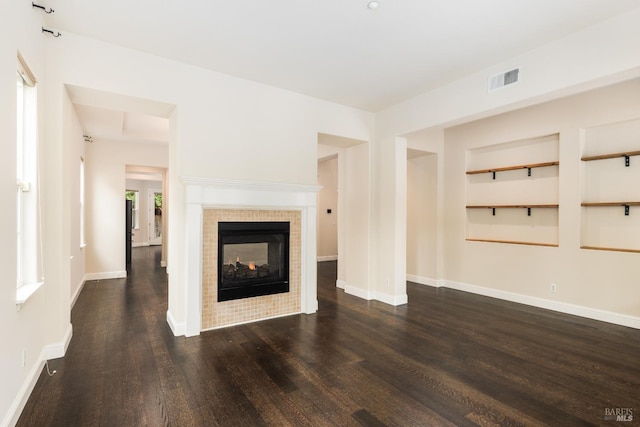 unfurnished living room featuring a multi sided fireplace, dark hardwood / wood-style flooring, and built in features