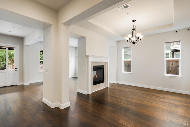 unfurnished living room featuring a multi sided fireplace, a raised ceiling, a chandelier, and dark hardwood / wood-style floors