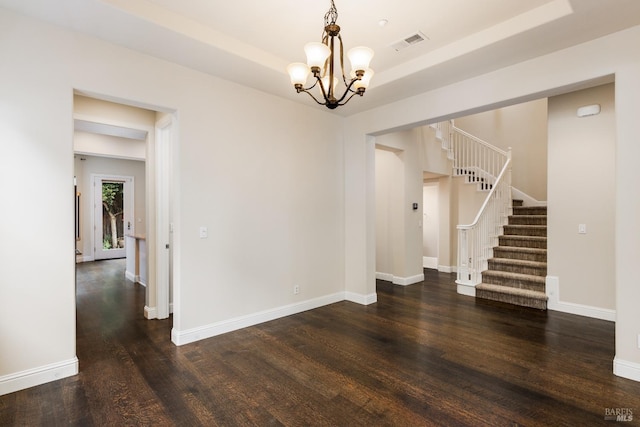 unfurnished room featuring a notable chandelier, a tray ceiling, and dark wood-type flooring