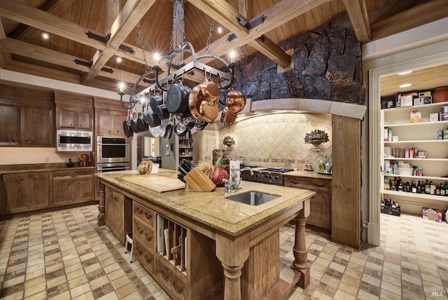 kitchen featuring beamed ceiling, sink, a center island with sink, stainless steel appliances, and wooden ceiling