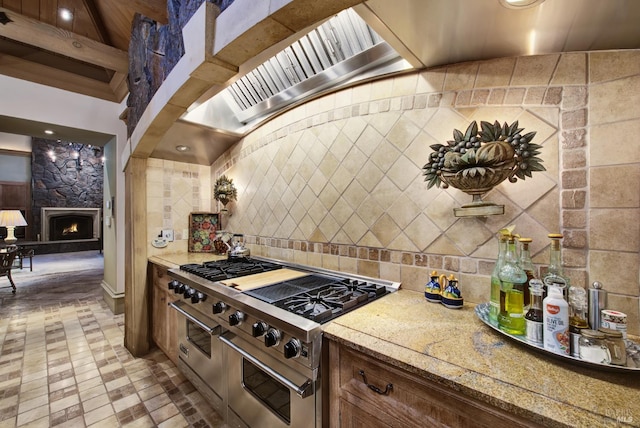 kitchen featuring high end stainless steel range, a stone fireplace, light stone countertops, and tile walls