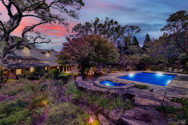 pool at dusk with an in ground hot tub and a patio area