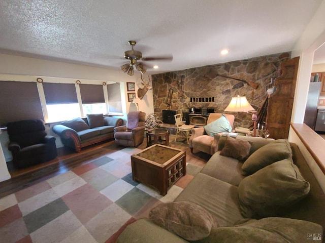 living room with ceiling fan, a stone fireplace, and a textured ceiling