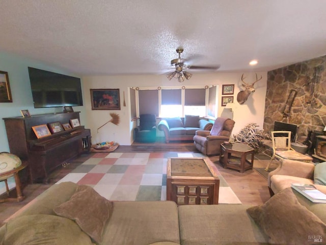 living room featuring a textured ceiling, ceiling fan, hardwood / wood-style flooring, and a stone fireplace