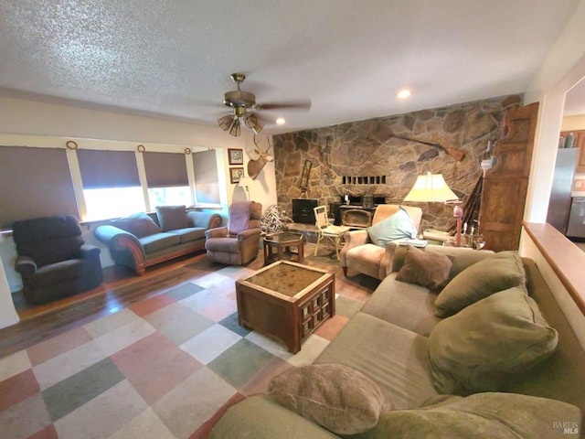 living room featuring a textured ceiling, ceiling fan, and a stone fireplace