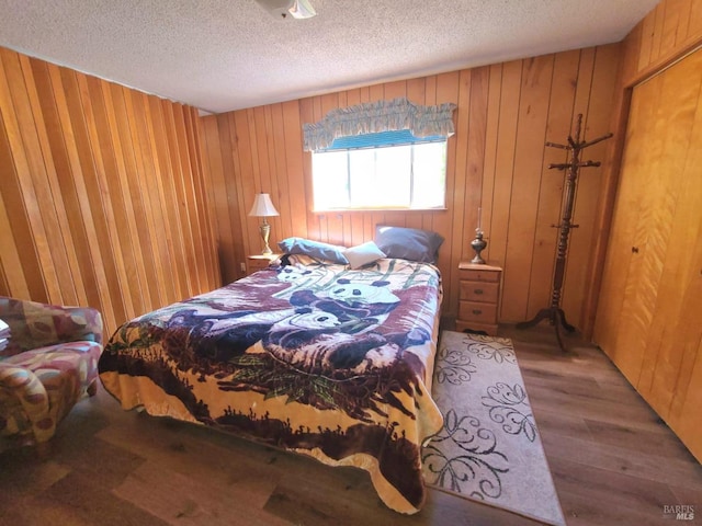 bedroom featuring a closet, wooden walls, a textured ceiling, and hardwood / wood-style flooring