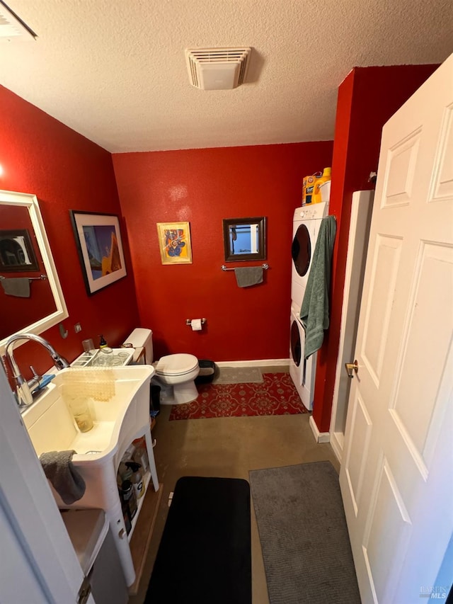 bathroom featuring a textured ceiling, stacked washer and dryer, sink, and toilet