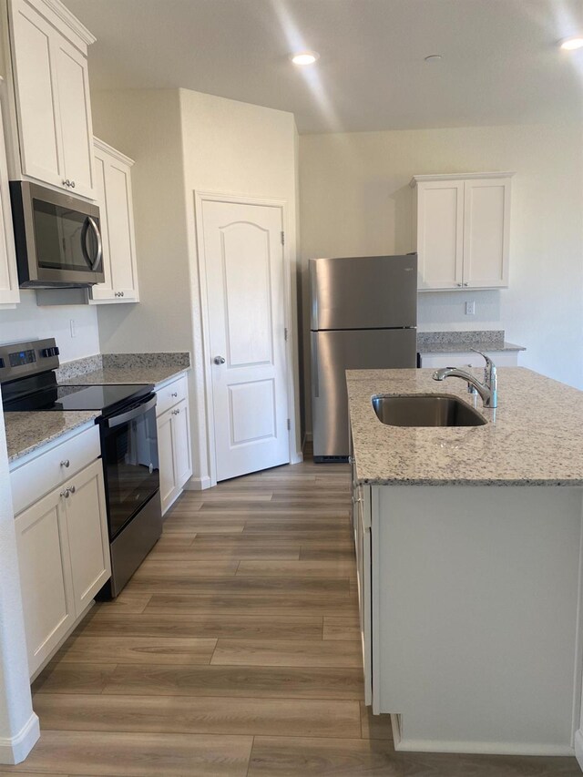 kitchen featuring sink, white cabinetry, stainless steel appliances, light stone counters, and a center island with sink