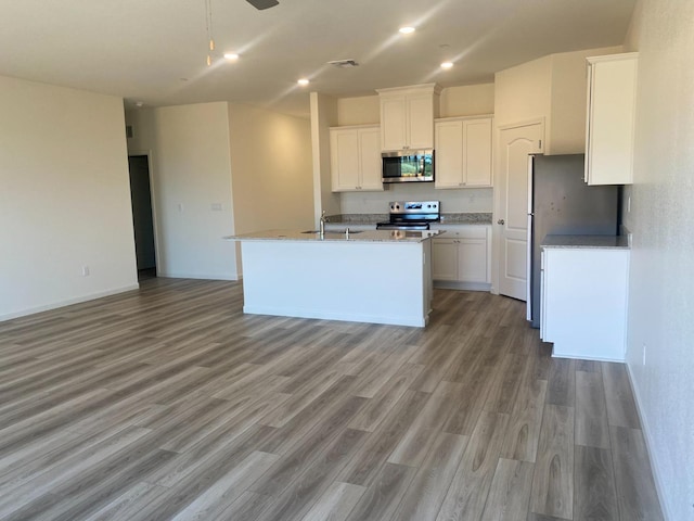 kitchen featuring white cabinets, ceiling fan, stainless steel appliances, a center island with sink, and light wood-type flooring