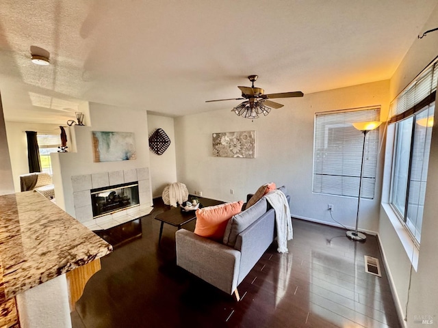 living room with a fireplace, a textured ceiling, dark hardwood / wood-style floors, and ceiling fan