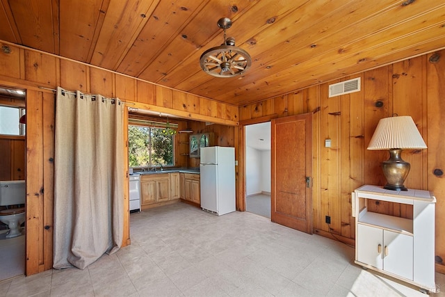 kitchen with hanging light fixtures, wood ceiling, white appliances, wooden walls, and sink