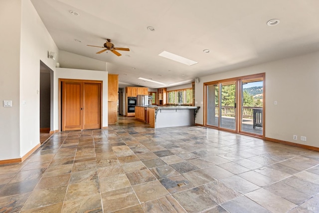 unfurnished living room with vaulted ceiling with skylight and ceiling fan