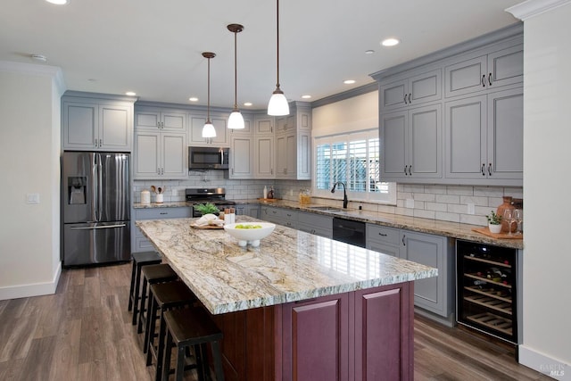 kitchen featuring wine cooler, a kitchen island, decorative light fixtures, appliances with stainless steel finishes, and crown molding