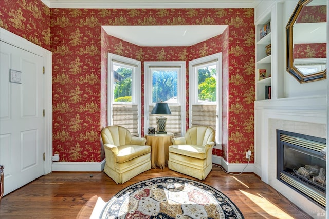 sitting room featuring built in shelves, crown molding, and dark wood-type flooring