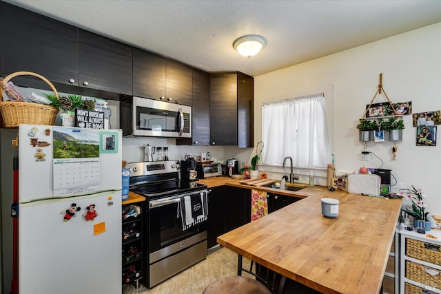 kitchen with a textured ceiling, sink, kitchen peninsula, stainless steel appliances, and wooden counters