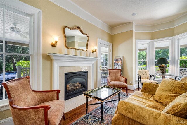 living room featuring ornamental molding, light wood-type flooring, ceiling fan, and a tile fireplace