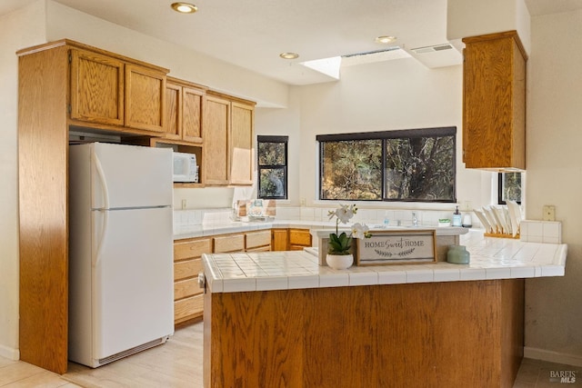 kitchen featuring white appliances, light hardwood / wood-style flooring, kitchen peninsula, and tile countertops