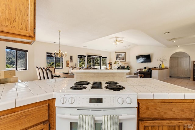 kitchen featuring tile counters, ceiling fan with notable chandelier, white range with electric cooktop, and vaulted ceiling