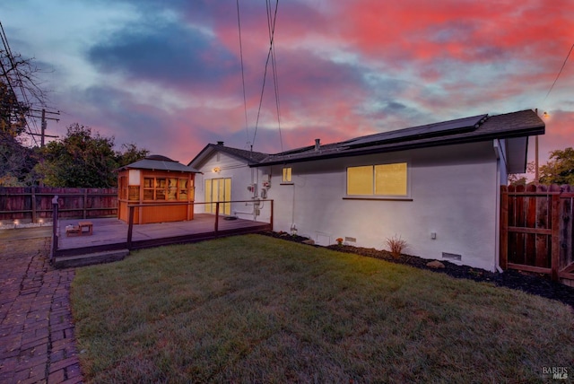 back house at dusk featuring a wooden deck, a yard, and solar panels