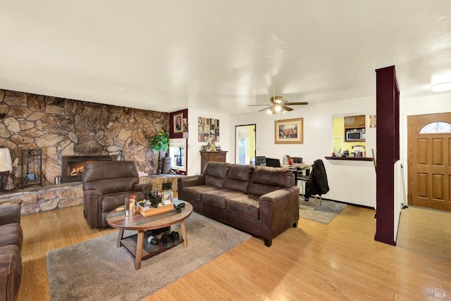 living room featuring a stone fireplace, ceiling fan, and light wood-type flooring