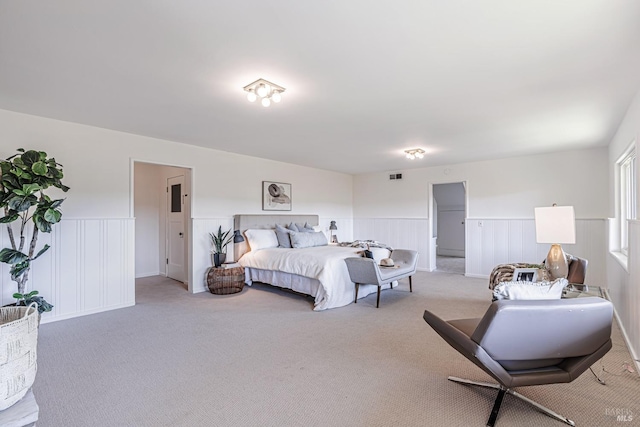 bedroom with light carpet, visible vents, and a wainscoted wall