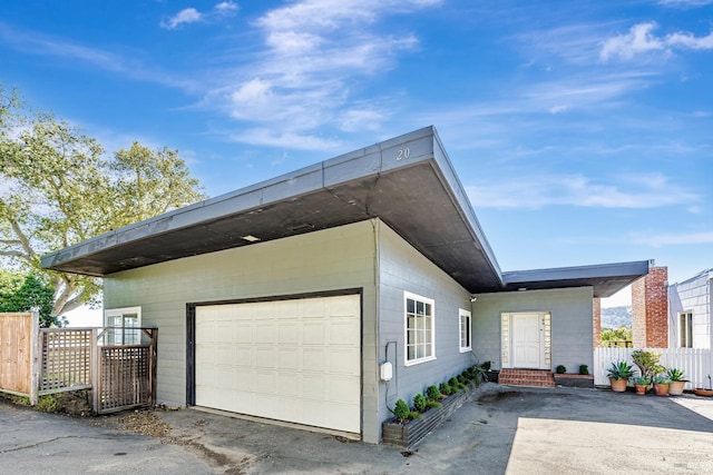 view of property exterior with driveway, an attached garage, fence, and entry steps