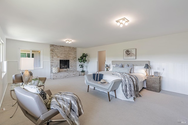 bedroom featuring a wainscoted wall, a stone fireplace, and carpet flooring