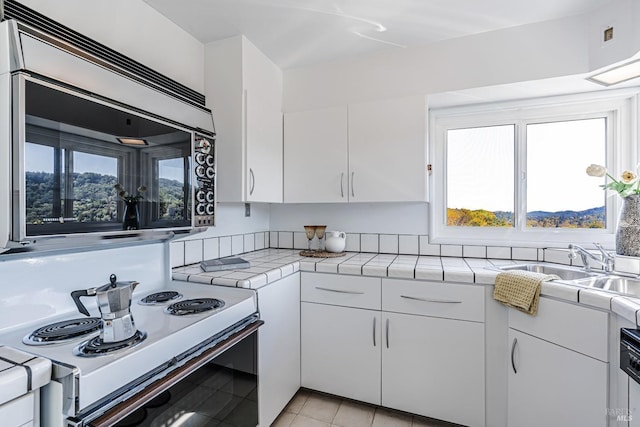 kitchen with a sink, white range with electric stovetop, tile counters, and a wealth of natural light