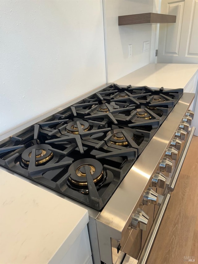 room details featuring stainless steel range with gas stovetop, hardwood / wood-style flooring, and white cabinetry