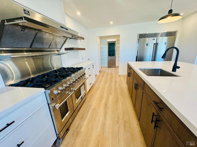 kitchen featuring sink, high end appliances, decorative light fixtures, exhaust hood, and light wood-type flooring