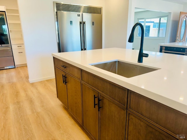 kitchen featuring stainless steel built in fridge, light hardwood / wood-style floors, and sink