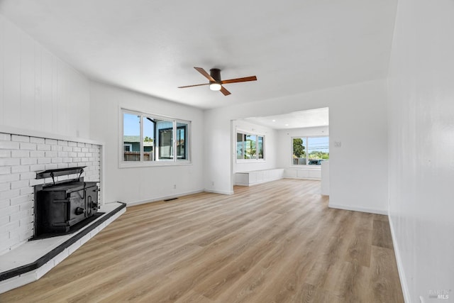 unfurnished living room with a wood stove, a brick fireplace, ceiling fan, and light wood-type flooring