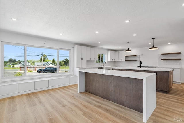 kitchen with a center island, sink, white cabinets, hanging light fixtures, and light hardwood / wood-style flooring