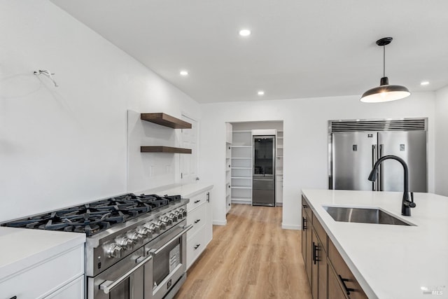 kitchen featuring white cabinets, sink, premium appliances, decorative light fixtures, and light hardwood / wood-style floors