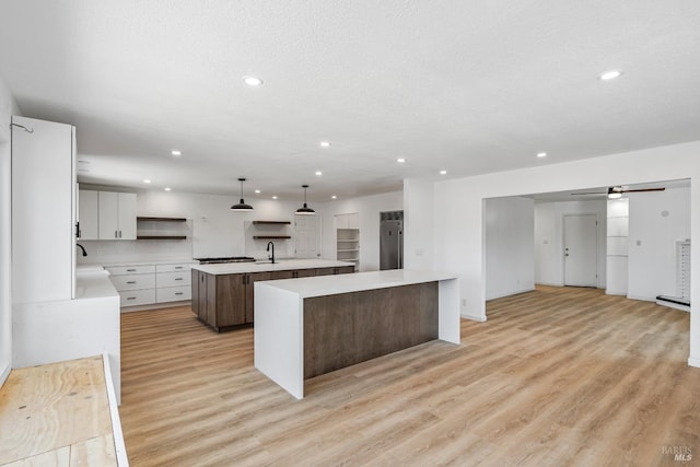 kitchen featuring pendant lighting, light wood-type flooring, a large island with sink, sink, and white cabinets