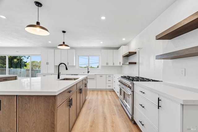 kitchen with hanging light fixtures, an island with sink, white cabinets, double oven range, and sink