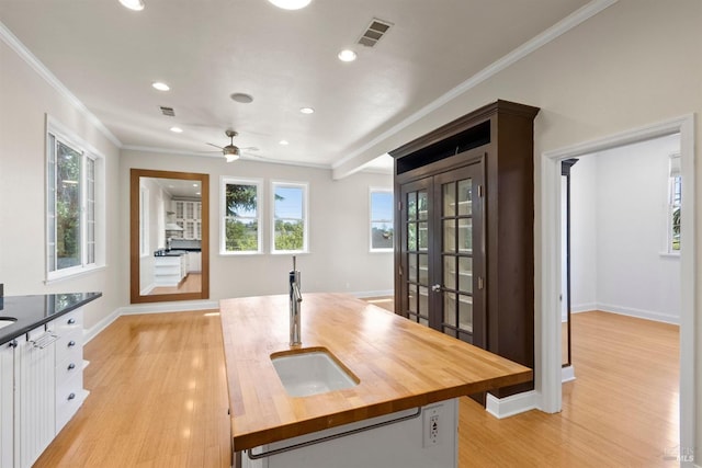 kitchen with white cabinets, light hardwood / wood-style flooring, a kitchen island with sink, wood counters, and sink