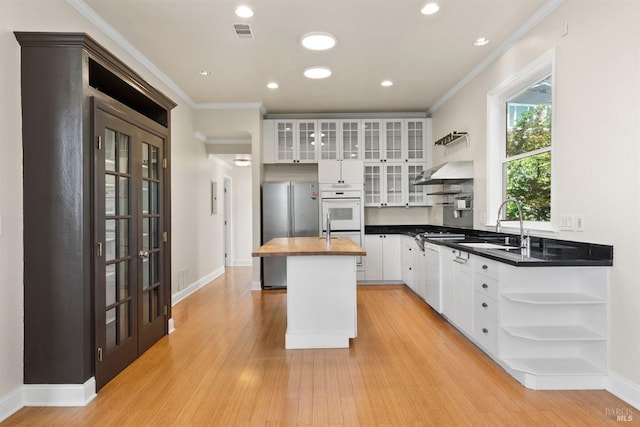 kitchen featuring light hardwood / wood-style floors, white cabinets, a kitchen island, stainless steel refrigerator, and crown molding