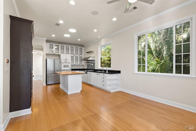 kitchen featuring stainless steel fridge, white cabinetry, butcher block countertops, oven, and a center island