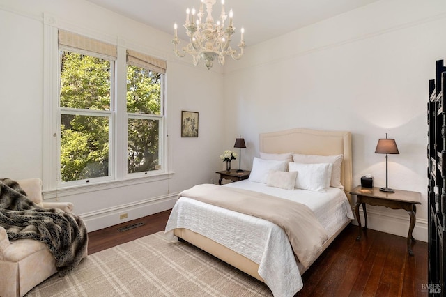 bedroom featuring baseboards, an inviting chandelier, wood finished floors, and visible vents
