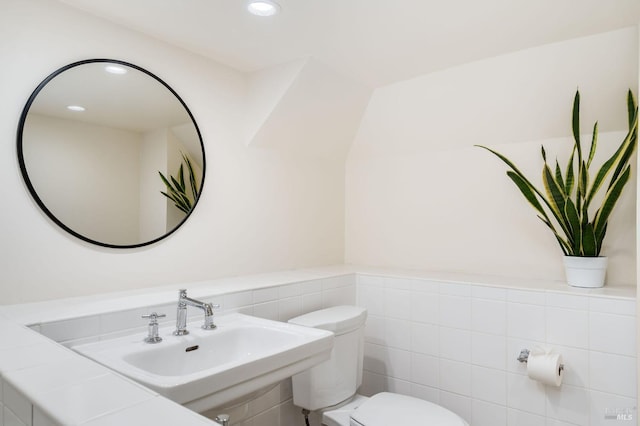 half bathroom featuring toilet, a sink, recessed lighting, and tile walls