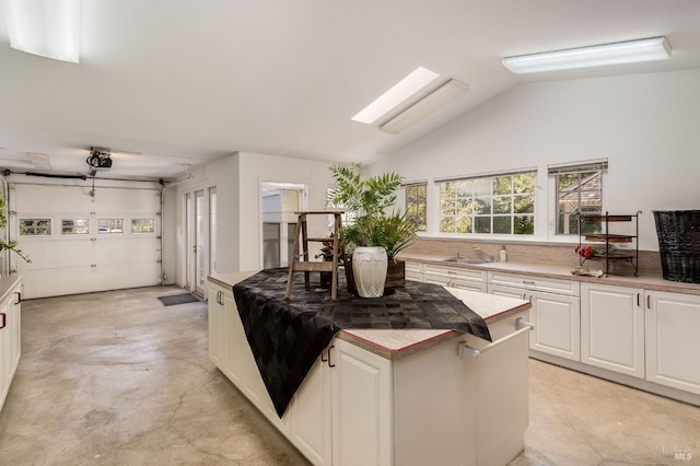 kitchen with concrete flooring, a center island, white cabinets, a sink, and vaulted ceiling