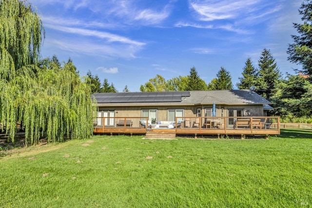 rear view of property featuring solar panels, a wooden deck, and a yard