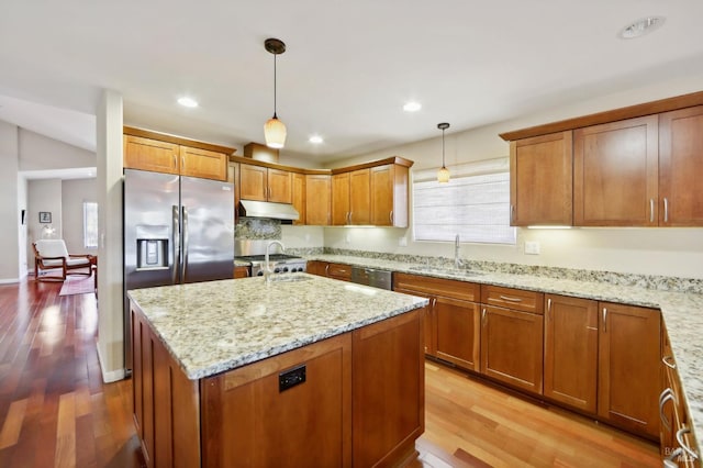 kitchen featuring hanging light fixtures, light stone counters, light hardwood / wood-style flooring, a kitchen island with sink, and sink