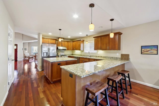 kitchen with light stone counters, dark hardwood / wood-style floors, kitchen peninsula, a kitchen island, and decorative light fixtures