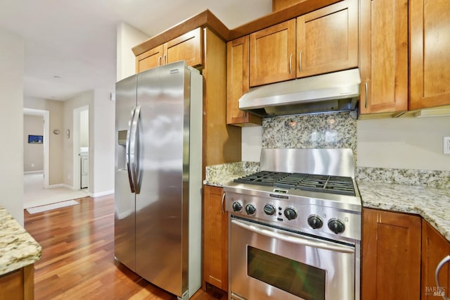 kitchen featuring light stone countertops, stainless steel appliances, light hardwood / wood-style floors, and washer / clothes dryer